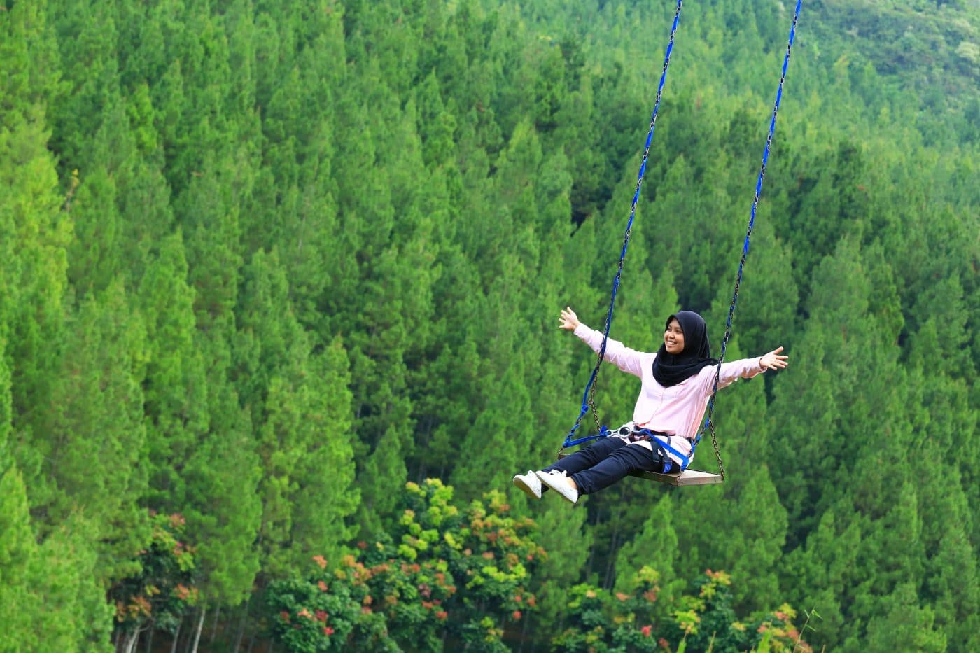Woman on swing above trees, smiling